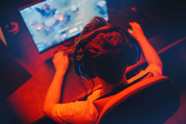 Jogador de vídeo profissional jogando torneios de jogos online pc computador com fones de ouvido, Desfocado fundo vermelho e azul - Foto, Imagem