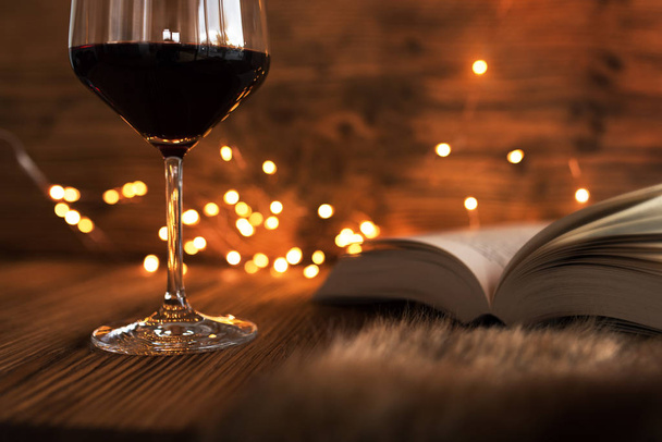 Glass of red wine with a good book and gold bokeh on a cozy winter evening - Valokuva, kuva