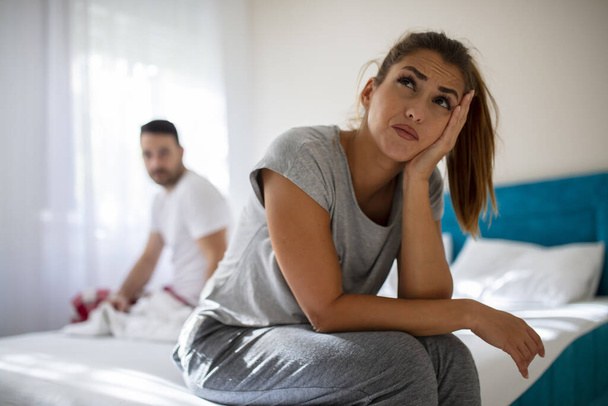 Couple having arguments and sexual problems in bed. Upset young couple having problems with sex. We have a problem. Young upset girl sitting on the edge of the bed, against her boyfriend. - Photo, Image