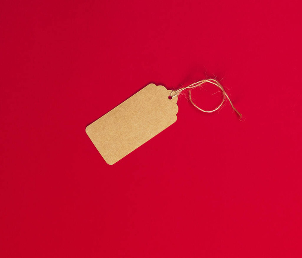 empty brown paper tag for clothes on a rope lies on a red background - Fotó, kép
