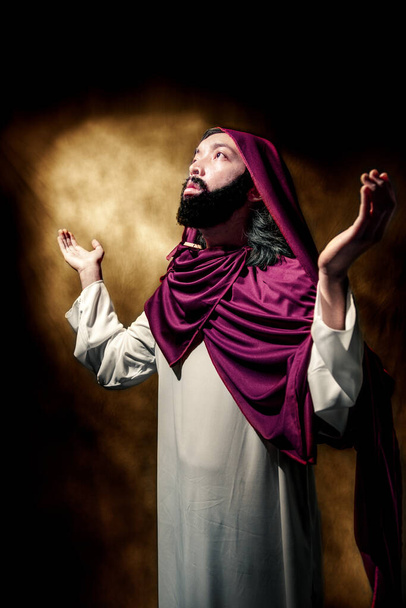 Jesus christ raised arms with open palm praying over dark background - Foto, Bild