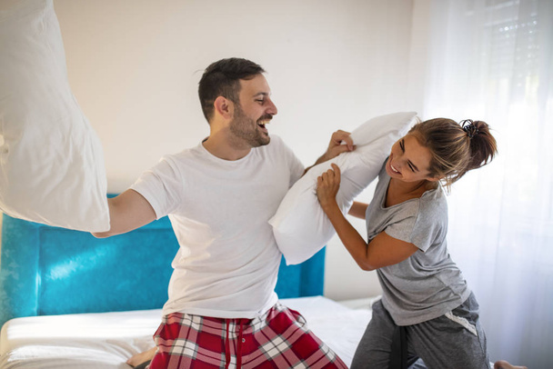 Cheerful funny young couple in love fighting with pillows. Lovely couple in pyjamas spending Valentine's day in their bed, having a pillow fight for entertainment. Couple fighting with pillows - Foto, immagini