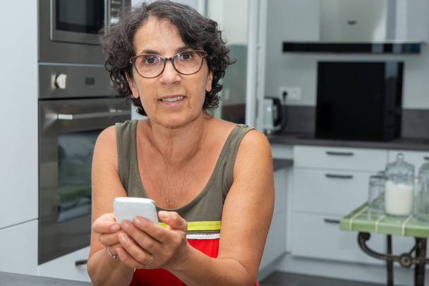 a beautiful mature woman using a smartphone in kitchen - Foto, Imagen