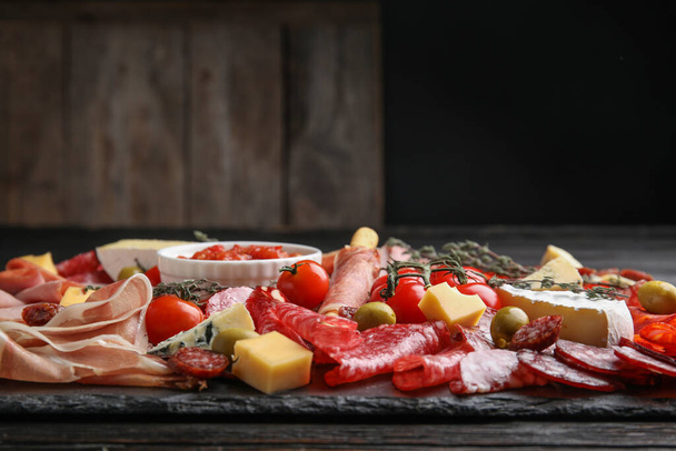 Tasty prosciutto with other delicacies served on black table - Foto, imagen