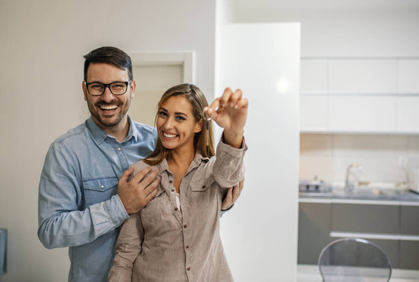 Couple showing keys to new home. Young couple holding up new house key. Portrait of young couple feeling happy about buying a new house. Happy couple moving in new home - Fotografie, Obrázek