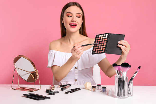 Beauty blogger with brush and eyeshadow palette on pink backgrou - Fotó, kép
