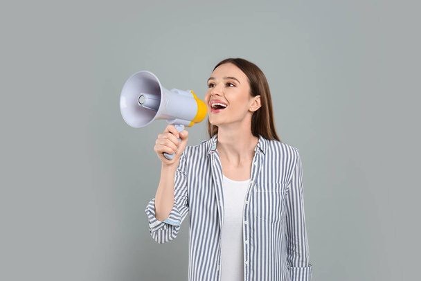 Young woman with megaphone on light grey background - Foto, imagen