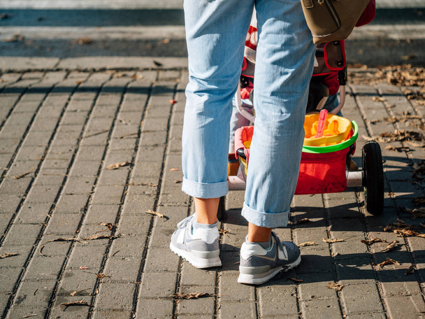 legs of a young woman in cropped jeans and sneakers, with a baby carriage near a pedestrian crossing - Photo, image