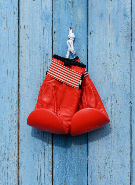 red leather boxing gloves hang on a nail on a blue wooden wall - Fotoğraf, Görsel
