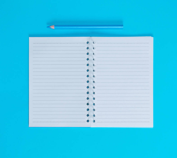 notebook with empty white sheets in line and blue wooden pencil, blue background, top view - 写真・画像