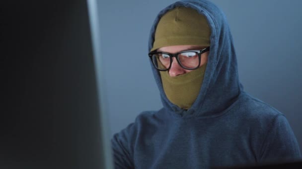Male hacker in the mask on face and glasses working on a computer in a dark office room. Cybercrime concept - Filmagem, Vídeo
