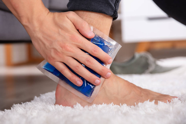 Close-up Of A Man Applying Ice Gel Pack On An Injured Ankle - Foto, Imagen