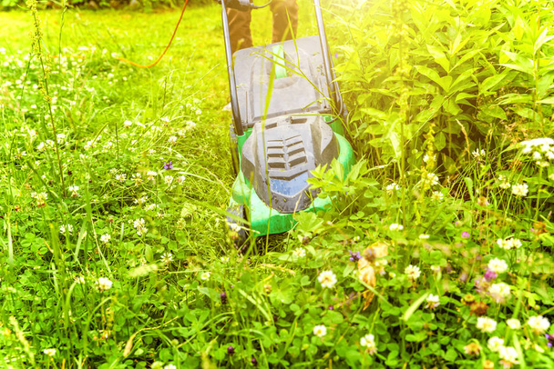 Человек стрижет зеленую траву газонокосилкой на заднем дворе. Садоводство деревенский образ жизни. Прекрасный вид на лужайку из свежей зеленой травы на солнце, пейзаж сада весной или летом. - Фото, изображение