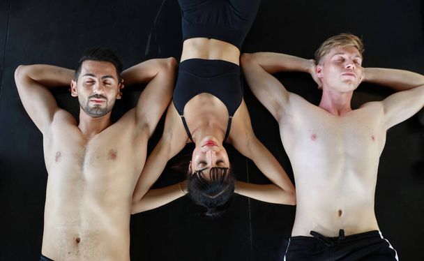 group of sporty caucasian woman and man in sport wear lying on fitness floor and resting from exercising in gym with sexy body and close their eyes - Foto, Bild