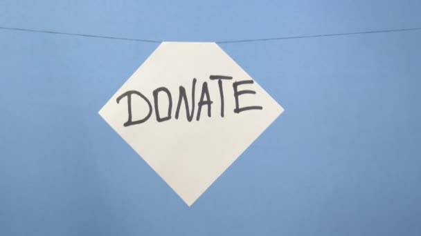 Burning and smoking white sheet of paper with a black inscription "donate" on a blue background - Séquence, vidéo