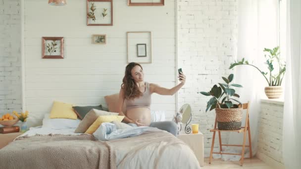Lächelnde Schwangere beim Selfie-Foto. werdende Mutter sitzt im Bett. - Filmmaterial, Video