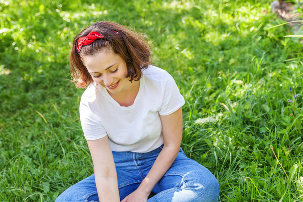 Happy girl smiling outdoor. Beautiful young brunete woman with brown hair resting on park or garden green grass background. European woman. Positive human emotion facial expression body language. - Foto, Imagem
