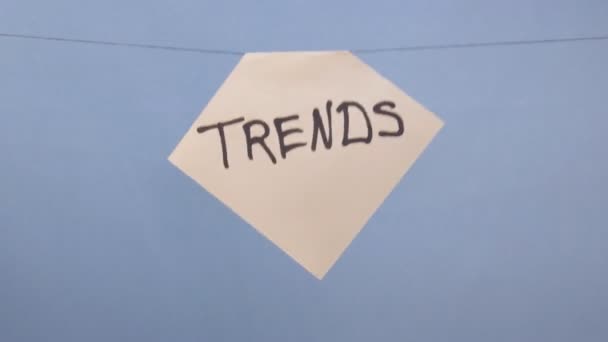 Een man hangt een wit vel papier met een zwarte inscriptie "trends" op een blauwe achtergrond - Video