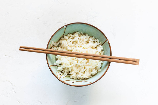 top view of wooden chopsticks above cup with boiled rice on white concrete board - Foto, afbeelding