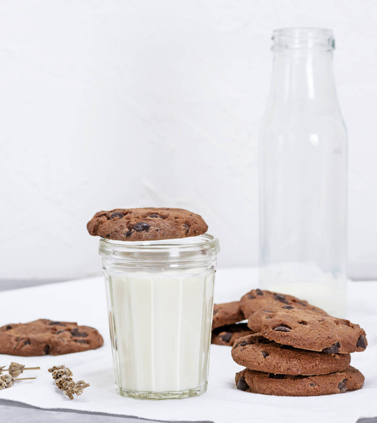 full glass of milk and round chocolate chip cookies, an empty milk bottle behind - Foto, imagen