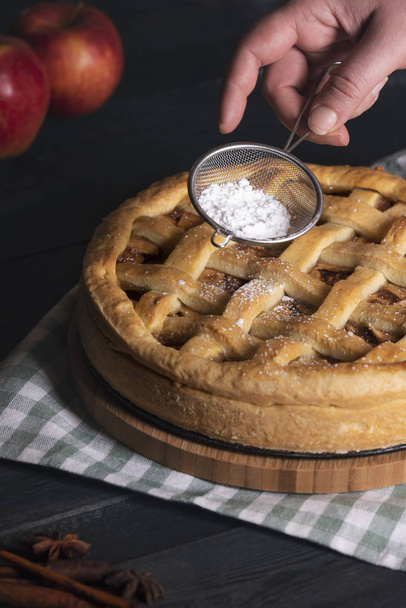 Home baking concept with a woman hands pouring powdered sugar from a sieve to a classic apple pie, on a kitchen table. Traditional sweet food. - Fotoğraf, Görsel