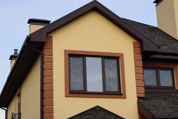 Ático marrón de una casa privada con una ventana grande debajo de un techo de azulejos en la calle contra un cielo azul. - Foto, Imagen