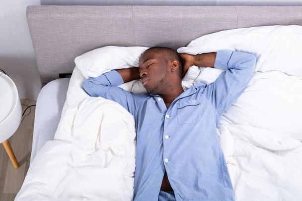 High Angle View Of Young African Man Sleeping On Bed In Bedroom - Foto, imagen
