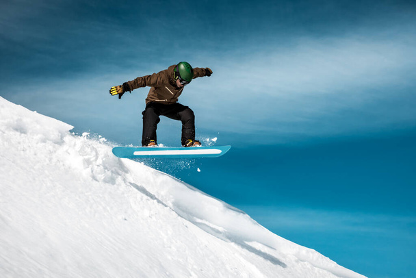 Snowboarder performs a trick on the slope in a snow-capped mountains, amazing sunny winter day, extreme wintertime holidays. - Foto, Bild
