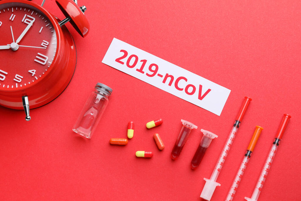 Reagenzgläser mit Blutprobe, Medikamenten gegen Coronavirus und Wecker auf farbigem Hintergrund - Foto, Bild