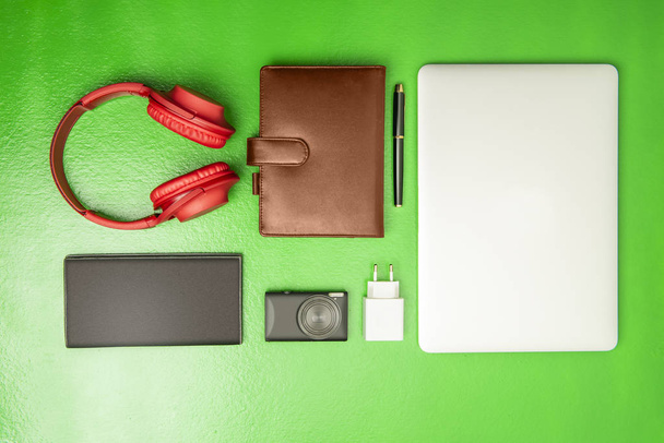 Businessman equipment like laptop, pen, notebook, camera, wallet and headphones for work on green background. View from above - Φωτογραφία, εικόνα