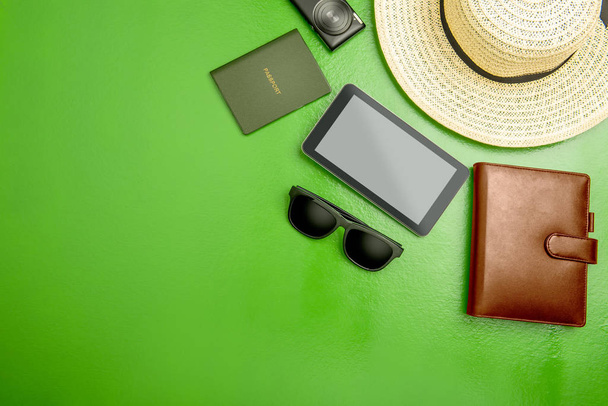 Accessories and equipment such as hat, wallet, camera, tablet, sunglasses and passport for traveling on green background. View from above - Foto, Bild