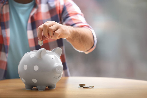 Man putting money into piggy bank at table, closeup. Space for text - Photo, Image