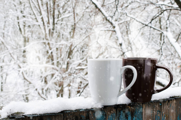 Cozy winter still life: Two Cups of Hot Coffee or Tea on a Snow Covered Terrace. Frosty winter day in forest. Christmas Holidays. Winter Cozy Background - 写真・画像