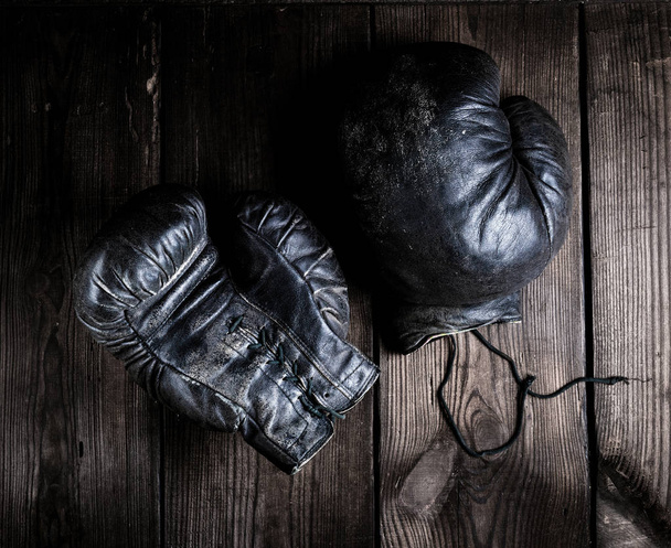 very old black boxing gloves on a brown wooden background, top view - Photo, Image