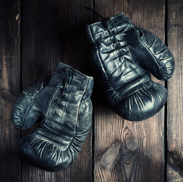 pair of black leather very old boxing gloves on a brown wooden background, vintage toning - Photo, image