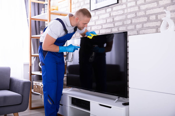 Young Male Janitor Cleaning Television With Soft Cloth - Φωτογραφία, εικόνα