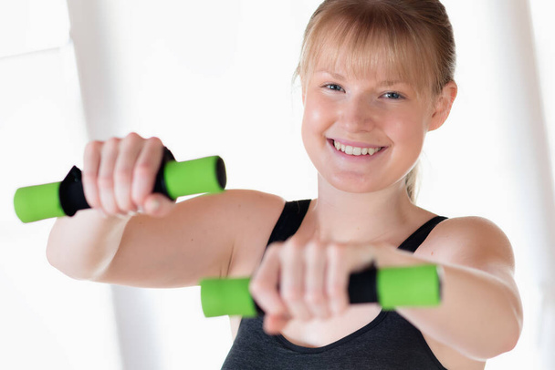 Young happy girl doing dumbbell exercises at home - Foto, Imagen