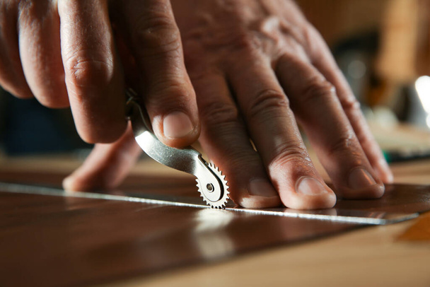 Man marking leather with roller in workshop, closeup - Фото, изображение
