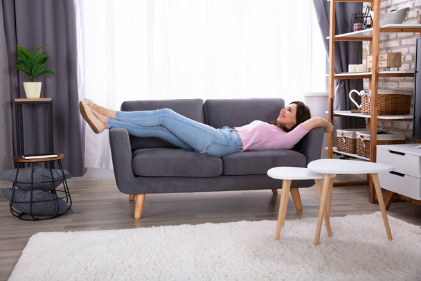 Smiling Young Woman Lying On Sofa At Home - Photo, image