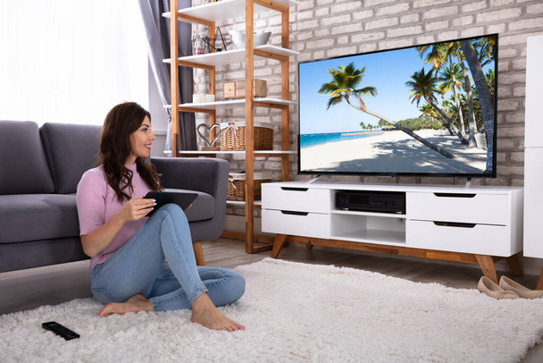 Happy Young Woman With Digital Tablet Sitting On Carpet Watching Television - Φωτογραφία, εικόνα