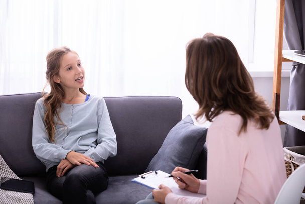 Girl Sitting On Sofa Explaining Her Problems To Female Psychiatrist At Home - 写真・画像