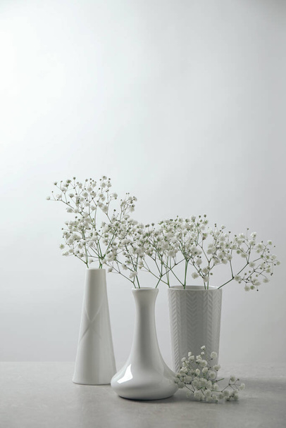 Gypsophila flowers in vases on table against white background - Фото, изображение