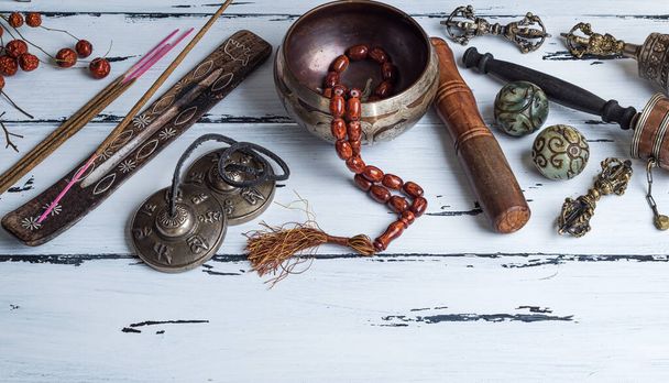 Copper singing bowl, prayer beads, prayer drum and other Tibetan religious objects for meditation and alternative medicine on a white wooden background - Photo, image