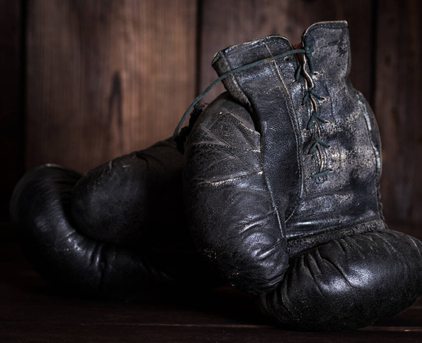 pair of very old shabby black leather boxing gloves on a brown wooden background - Photo, Image