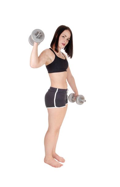 A beautiful young woman standing in her exercising outfit in profile.working out whit dumbbells, bare feet, isolated for white background. - Photo, Image