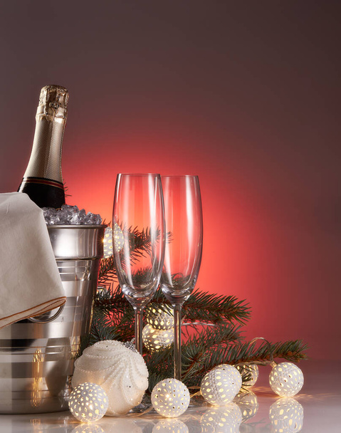Still life with champagne bottle standing in a bucket with ice, two empty champagne flutes, LED lights garland  and Christmas ornaments. Christmas and New Year celebration background - Φωτογραφία, εικόνα