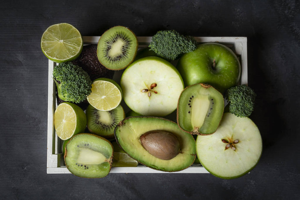 Fresh green fruits and vegetables in a wooden tray on the kitchen table. Above view with healthy food - Fotografie, Obrázek