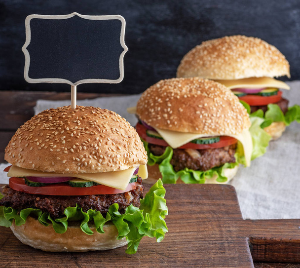 hamburger with meat patty and fresh vegetables, an empty wooden signpost is set on top - Foto, Imagen