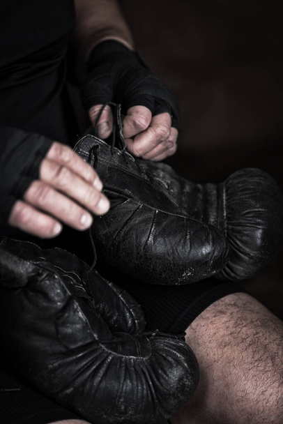 athlete puts on black leather boxing gloves before a fight, selective focus - Foto, afbeelding