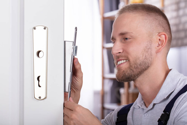 Close-up Of A Smiling Young Man Fixing Door Lock In House - Fotografie, Obrázek